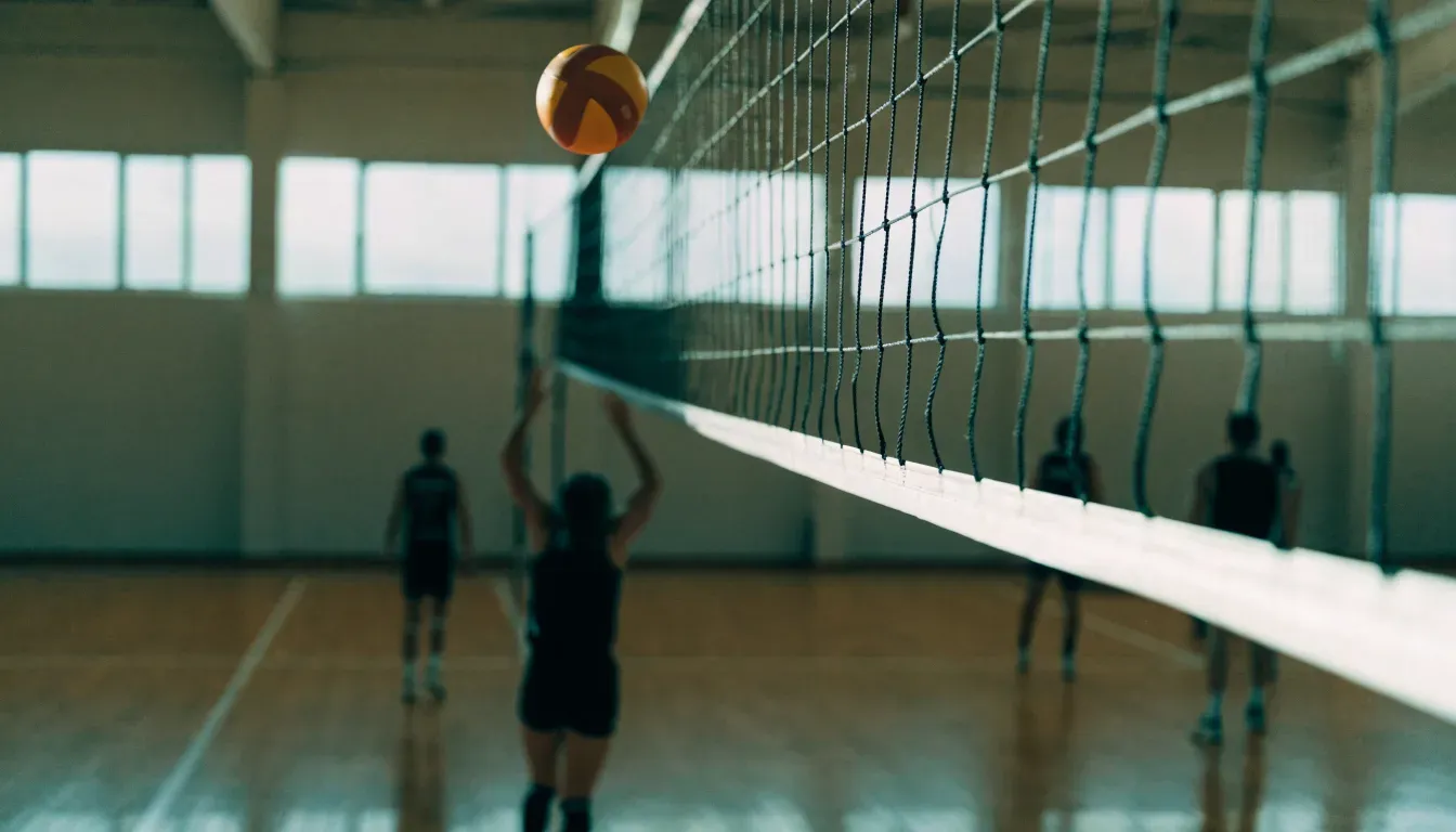 Eine Sporthalle mit gespanntem Volleyballnetz über poliertem Holzboden, hohe Fenster lassen Tageslicht herein.