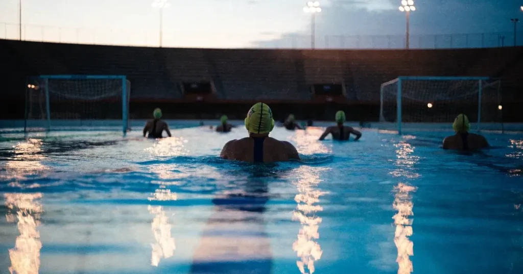 Ein Wasserballbecken am Abend mit zwei schwimmenden Torrahmen an den Enden, ruhiges blaues Wasser, leere Ränge.