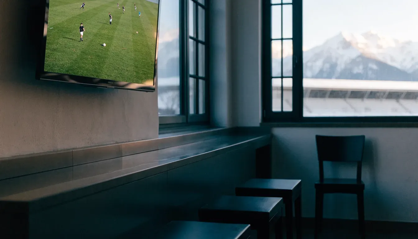 Schneebedeckte Berggipfel erheben sich im klaren Morgenlicht hinter einem leeren Stadion mit hellen Zuschauerrängen.